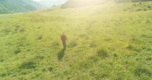 Flight Over Backpack Hiking Tourist Walking Across Green Mountain Field. Huge Rural Valley at Summer