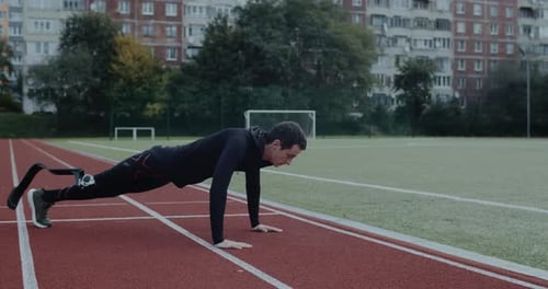 Strong Disabled Male Sportsman with Prosthetic Running Blades Doing Push Ups at Sports Field