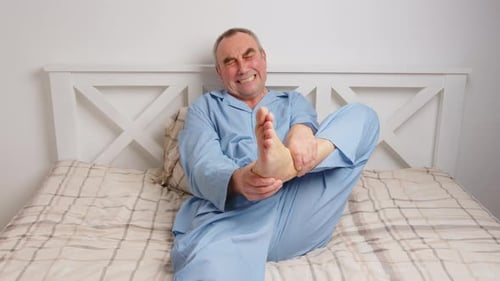 Senior Man Massaging Foot in Bed in Pain