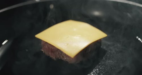 Hands Adding Cheese to Sizzling Burger in Pan