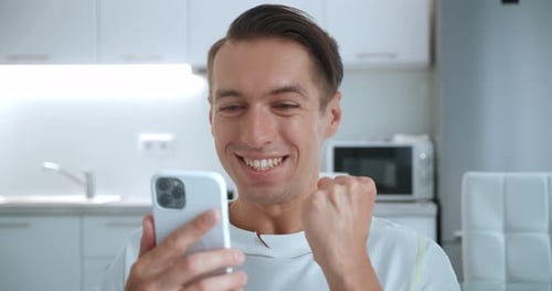 Man Reacts to Good News on Smartphone Indoors