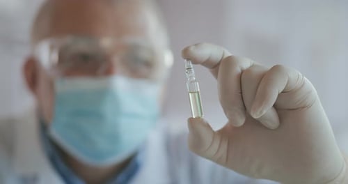 Close Up of the Developer of the Coronavirus Vaccine Holding an Ampoule of White Liquid Examining