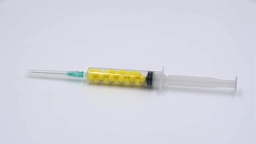 Syringe Filled With Yellow Pills on White Surface