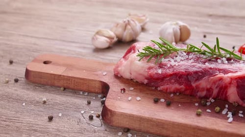 Raw Steak with Rosemary and Garlic on Cutting Board