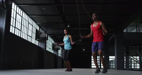 African american man and woman skipping rope in an empty urban building