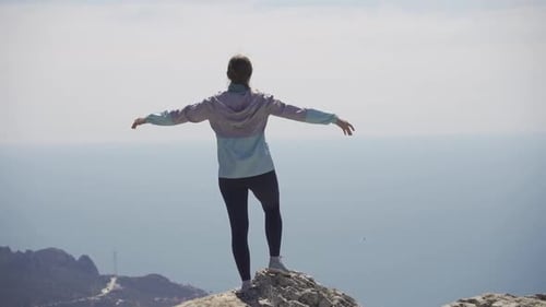 A Woman Stands on a Rock Looks Into the Distance and Spreads Her Arms to the Sides