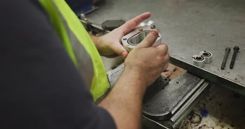Nahaufnahme der Hände eines kaukasischen Fabrikarbeiters, der an einer Werkbank steht und an einem arbeitet