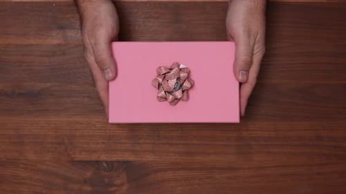 Hands Placing Pink Gift with Bow on Wood Table