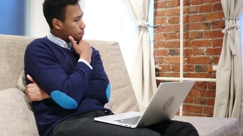 Thoughtful Young Adult With Laptop on Sofa