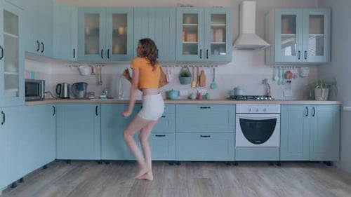 A Beautiful Woman in White Shorts is Relaxing at Home Dancing in the Kitchen