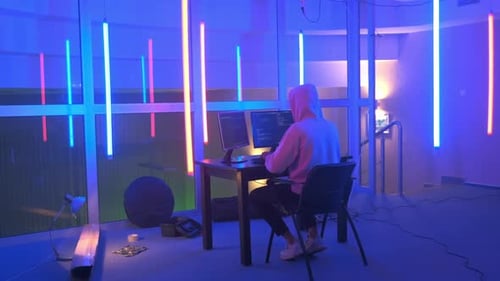 Lieu de travail d'un hacker : hacker travaillant dans une pièce avec des néons colorés