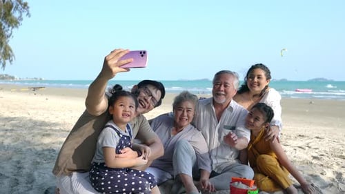 4K Asian family using mobile phone taking selfie together at the beach.