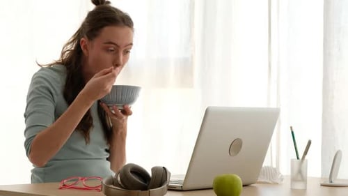 Woman Eating at Desk with Laptop and Headphones