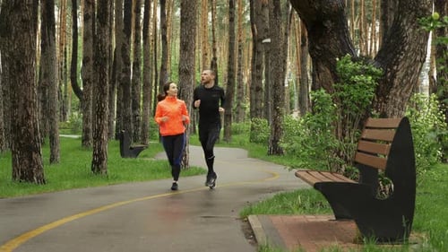 Young couple jogging on footpath in the park on rainy day. Man and woman running together.
