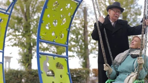 Senior couple on a playground, swinging on the swing set.