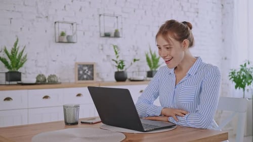 Woman Video Chats Using Laptop in Modern Kitchen