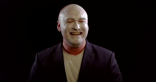 Man with White Makeup on Face Is Laughing Like a Joker in Black Background, Evil Uncontrollable