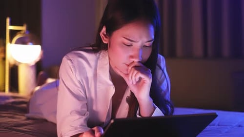 Young Asian beautiful woman enjoy using smartphone- tablet in bedroom at night time.