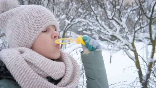 Young Girl Blowing Bubbles in the Snowy Winter