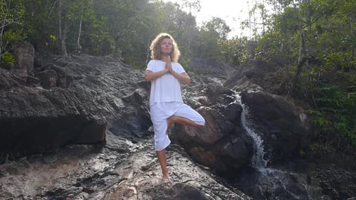 Woman Balances in Yoga Tree Pose Near Waterfall