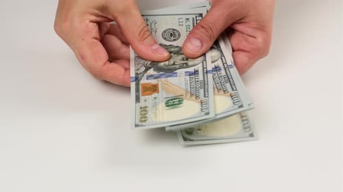 two female hands are laying on a white table a stack of paper hundred US dollar