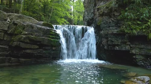 Waterfall on mountain river with white foamy water falling down from rocky formation