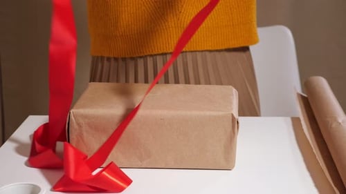 Woman wraps brown present with bright red ribbon