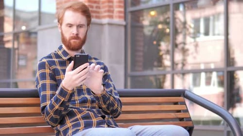 Man Typing Message on Smartphone Sitting Outdoor on bench