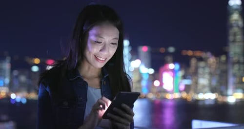 Woman Using Smartphone in Vibrant City at Night