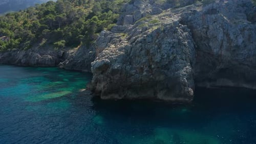 Drone Arcing Around Rocky Cliff Coastline And Blue Sea Of Ibiza
