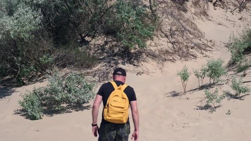 Barefoot Man with Backpack Hiking in Coastal Hot Sand Dunes Towards Beach