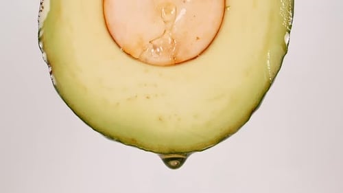 Macro Shot of Fresh Cut Avocado with Juice and Oil Stream on White Background