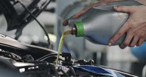 Hände des Mechanikers. Motoröl fließt aus dem Kanister in den Motor eines Autos.