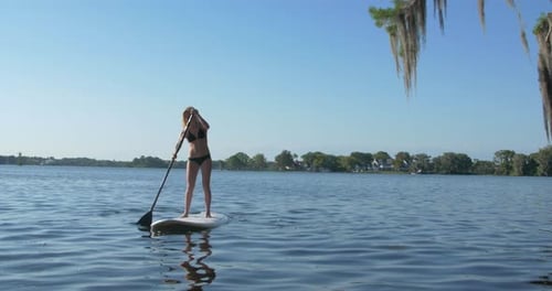 A young woman sup stand-up paddleboarding on a lake.