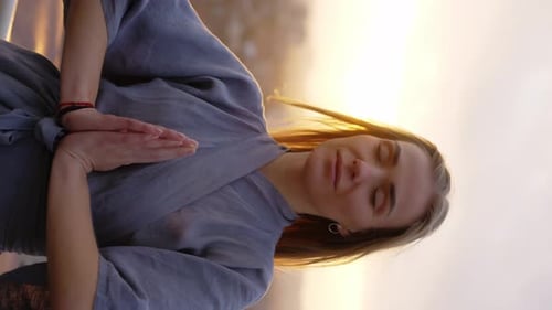 Friedliche blonde Frau steht auf der Terrasse mit geschlossenen Augen Namaste-Geste