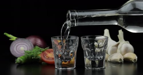 Versez la vodka alcoolisée d'une bouteille dans deux verres à shot. Fond avec des légumes