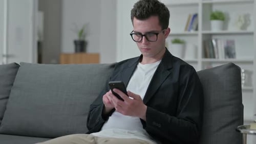 Young Adult Uses Smartphone While Relaxing on Couch