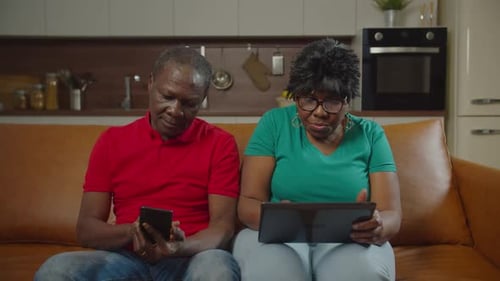 Couple Using Tablet and Smartphone on Couch