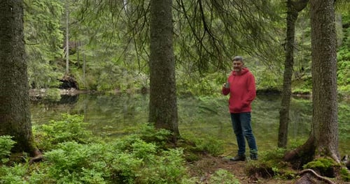 Bearded Man Drinks Tea From a Mug Near a Mountain Lake