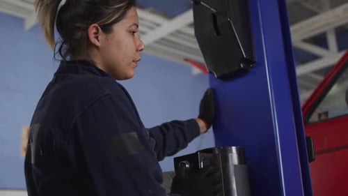 Mecánica levantando un automóvil con una grúa automática presionando un botón en una estación de servicio de automóviles