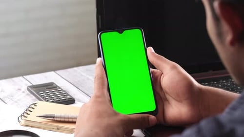 Rear View of Young Man Using Smart Phone and Laptop on Table