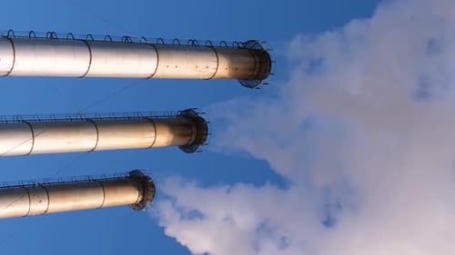 Industrial Smokestacks Against Blue Sky Ejecting Smoke