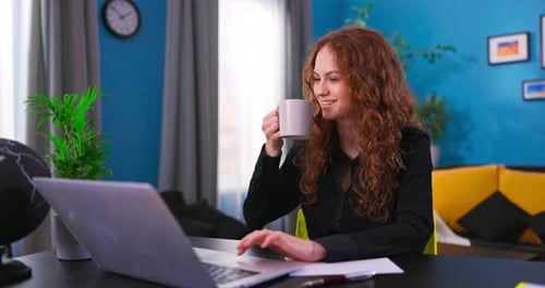 Beautiful Female Sitting at Desk in a Cozy Living Room and Following a Video School