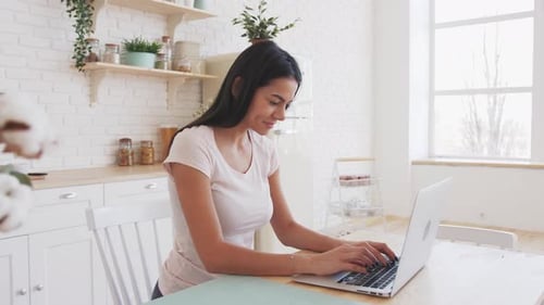 Young Woman Typing on Laptop in Bright Kitchen