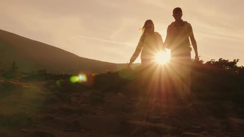 A Young Couple of Tourists with Backpacks Walking Along a Mountain Trail