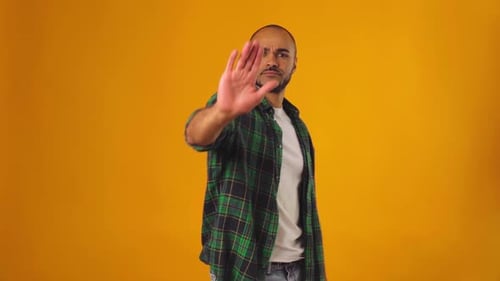 Young African American Man in Green Shirt Showing Stop Sign with His Hand Against Yellow Background