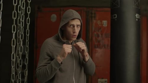 Hooded Man Boxing with Punching Bag Indoors