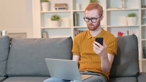 Young Adult on Couch Using Phone and Laptop