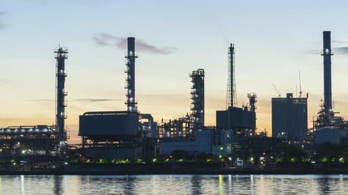 4K-Zeitraffer der petrochemischen Anlage einer Ölraffinerie bei Sonnenaufgang mit Spiegelung des Flusses