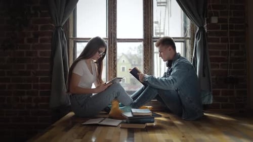 Young Adults Reading Tablets on Window Ledge